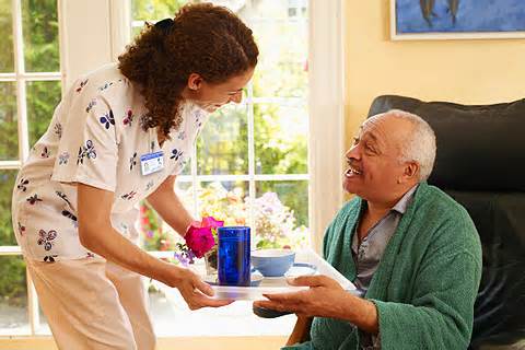 A nurse is handing an elderly man some tea.